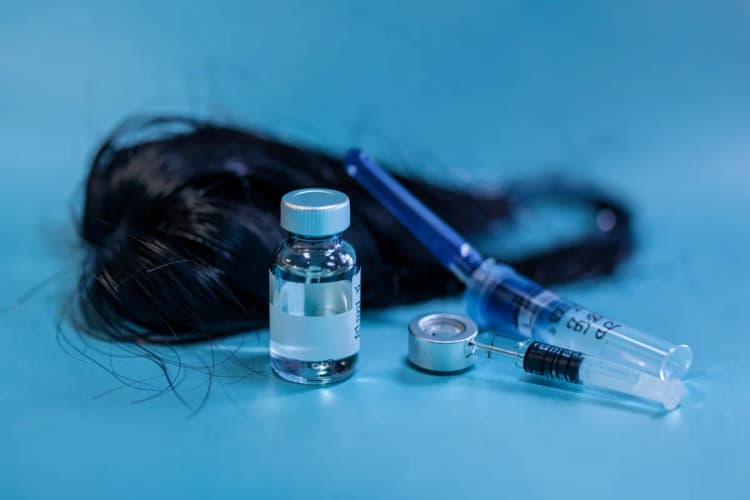 Um frasco de medicamento com conta-gotas e uma seringa ao lado de um couro cabeludo com poucos fios de cabelo.