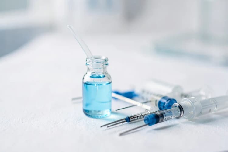Frasco de medicamento com conta-gotas ao lado de agulhas e seringas sobre fundo branco.
