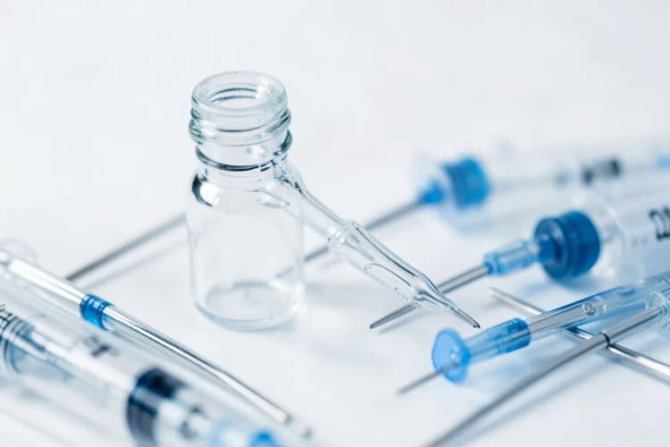 Frasco de medicamento com conta-gotas ao lado de agulhas e seringas sobre fundo branco.