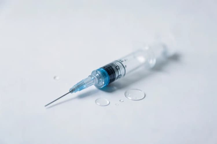 Uma seringa com agulha fina sobre uma superfície branca com algumas gotas de líquido ao lado.