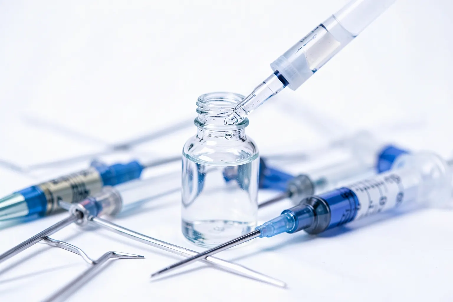 Frasco de medicamento com conta-gotas ao lado de agulhas e seringas sobre fundo branco.