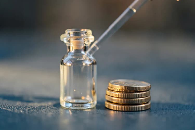 Frasco de medicamento com conta-gotas e uma pequena pilha de moedas ao lado