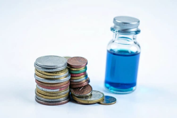 Uma pilha de moedas de diferentes tamanhos e cores ao lado de um frasco de medicamento com conta-gotas