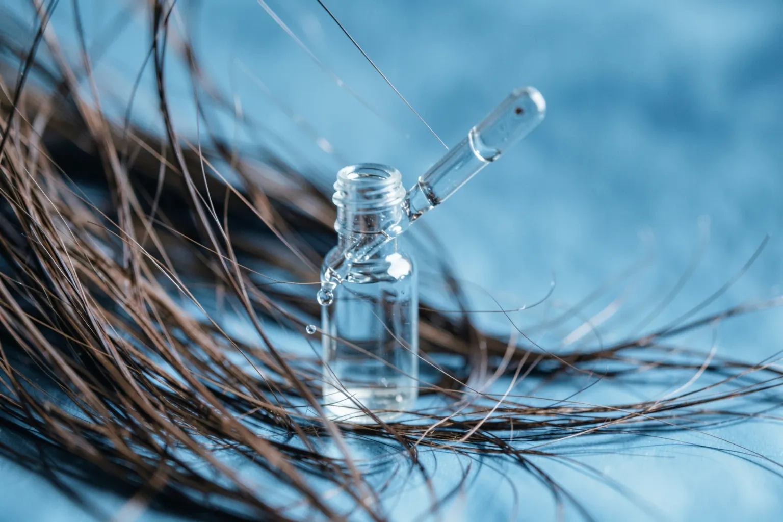 Frasco de medicamento com conta-gotas ao lado de cabelo castanho caindo em câmera lenta